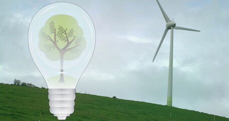 Image of tree in light bulb over wind turbine in green landscape
