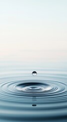 A pristine water droplet creates ripples in a tranquil setting at dawn, capturing a moment of serene beauty on the surface of a calm lake