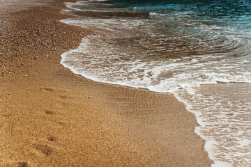 Beautiful wave on sandy beach with footprints