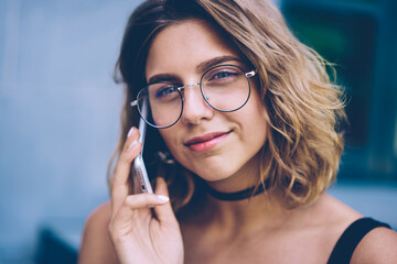 Prosperous millennial hipster girl in trendy sunglasses making positive friendly telephone call via application on cellphone, close up portrait of smiling woman talking with colleague via cellular