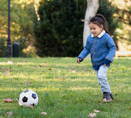 Small hispanic boy playing in a park with a soccer ball in autumn