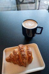 Latte art in a small blue porcelain mug with a partially eaten croissant in a small cafe in Calgary, AB, Canada.