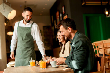 Waiter serves delicious vegetarian dishes to cheerful diners in a vibrant café during a sunny...