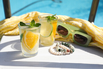 Tasty cocktail in glasses and sunglasses near swimming pool outdoors