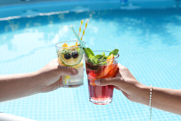Women holding tasty cocktail in glass near swimming pool outdoors, closeup