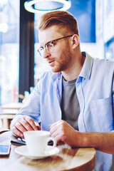 Serious male and female owners of cozy cafeteria creating schedule for workers and making notes in textbook while sitting at table with cup of coffee, concept of entrepreneurship and cooperation