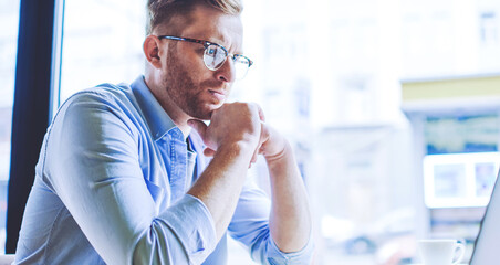 Serious male software developer working remotely in cafe interior with good wifi connection checking program code in laptop application and feeling pondering on mistakes, concept of distance job
