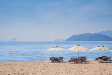 Beach umbrellas with sun beds on sandy beach by sea at the resort during the day in summer