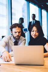 Concentrated diverse male and female office workers analyzing information on financial website on laptop during brainstorming, concept of teamwork and collaboration. Two colleagues cooperating in team
