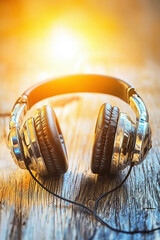 Fototapeta premium Stylish headphones resting on a wooden surface, illuminated by warm sunlight, symbolizing music and relaxation in a cozy atmosphere.