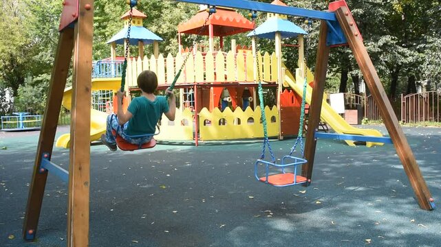 boy, child swinging on swing at playground in summer	
