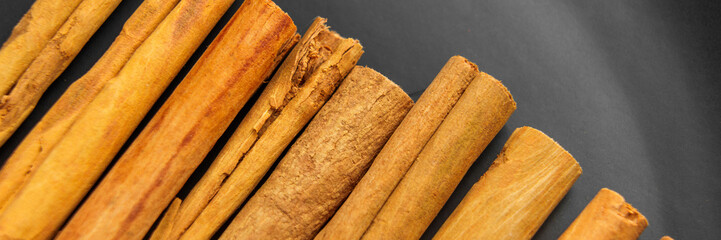 Fresh cinnamon stick stacked in a row on a black surface. Organic aromatic spice. Macro shot. Top view