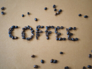 Auf einem hellbraunen Untergrund steht mit Kaffeebohnen geschrieben das Wort: COFFEE, einzelne...