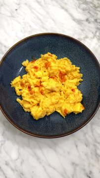 Dressing a plate of delicious and creamy scrambled eggs with red hot sauce.