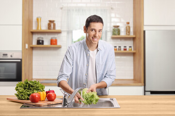 Young man washing vegetables in a kitchen sink