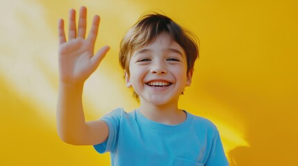 A cheerful young boy in a blue t-shirt waving his hand against a bright yellow background.