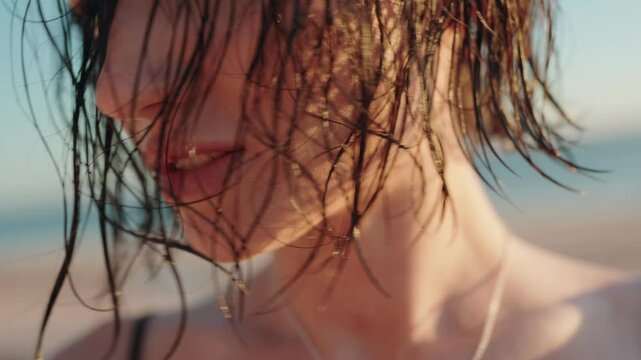 Close-up shot of a beautiful woman with wet hair on the beach. She is smiling and enjoying the sun.