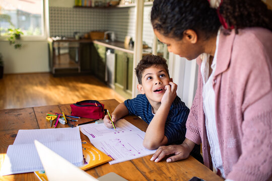 Mother helping son with homework at kitchen table during study time