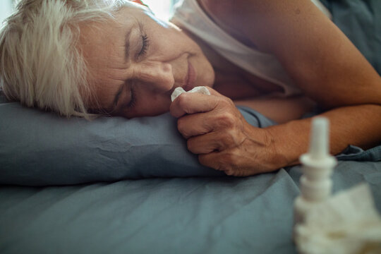 Senior woman with cold blowing nose in bedroom