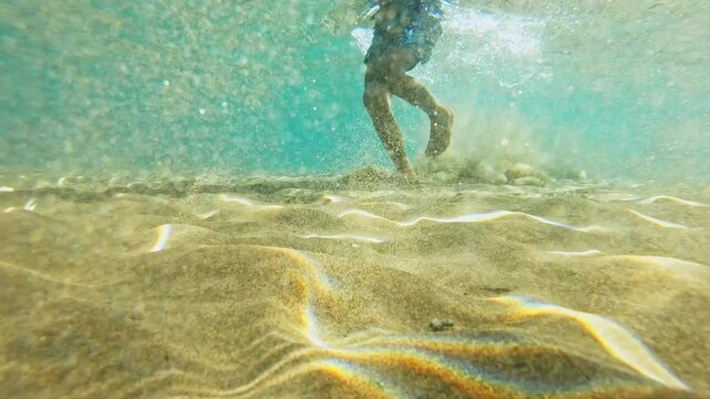 close up with bare feet of a child in the water swimming and running lifting the sand from the bottom of the sea. Child bare foot in the water. Baby swims with inflatable coil - underwater view.