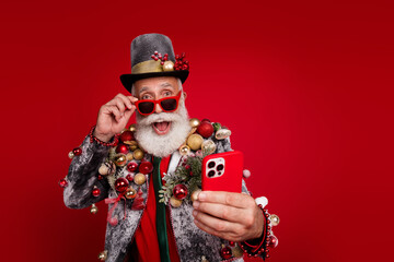 Photo of happy cheerful old man excited hold device wear christmas tree balls costume sunglasses...