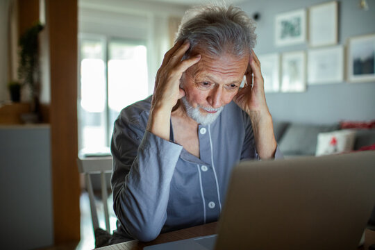 Frustrated senior man looking at laptop screen at home