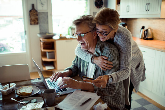 Happy mature couple using credit card on laptop at home