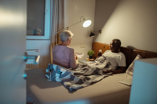 Elderly interracial couple managing finances in bed with laptop