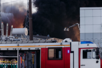 Firefighters use telescopic tower during massive large blaze fire, firetruck with crane, firemen team putting out the fire with extendable fire ladder, blazing warehouse factory, burning building