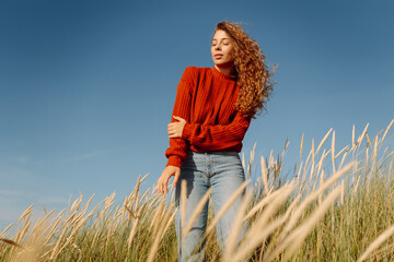 Beautiful woman enjoying nature outdoors in tall grass while wearing a cozy red sweater....
