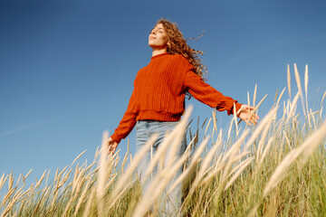 Beautiful woman enjoying nature outdoors in tall grass while wearing a cozy red sweater....