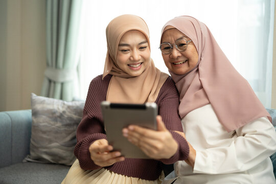 Two muslim mother and daughter using tablet in a living room at home - Powered by Adobe
