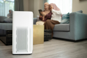 Air purifier in a living room. Muslim mother and daughter using tablet and open air purifier for fresh air, Air pollution concept