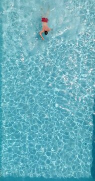 Top down view of a man in red shorts swimming in the pool, slow motion.