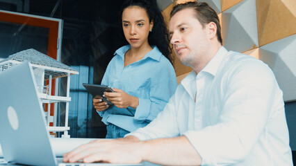 Portrait of project manager pointing at house model while discussion about building design. Caucasian cooperative architect engineer team brainstorming about building material. Teamwork. Manipulator.