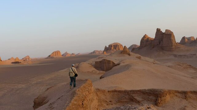 A lone man watches from a hilltop at sunrise among the Kaluts in the Lut Desert Iran