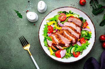 Foodie food salad with grilled duck and vegetables, lettuce and arugula on green background, top view