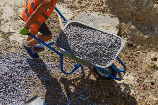 A worker is driving a wheelbarrow filled with gravel at a construction site, working with gravel at a construction site, loading and delivery of gravel.