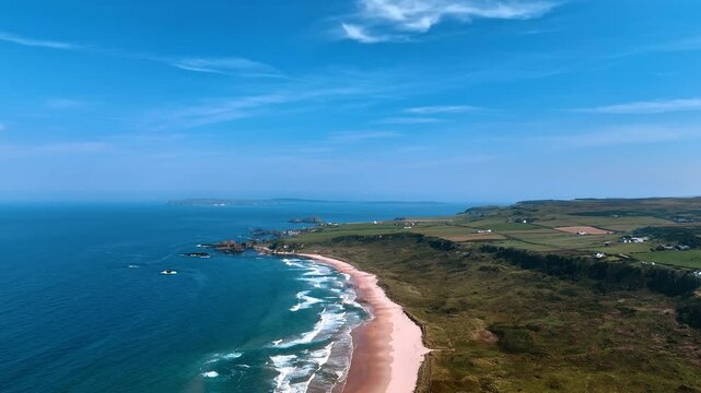 Capturing scenery of the Atlantic ocean at the coast of Ireland. Sandy beach and green valley with some houses and farm fields on from drone footage.