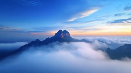 Obraz premium A stunning mountain peak emerges from dense morning mist, bathed in the soft glow of dawn, highlighting the serene beauty of high altitudes and nature's wonders