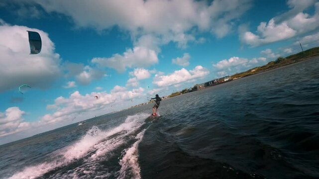 Male kitesurfer races along the coast holding a trapeze with one hand. Slow motion drone footage of the athlete