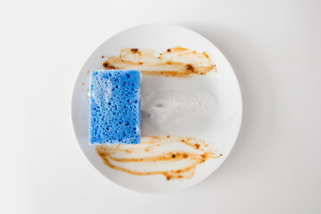 White round dirty plate with red sauce, foam plate cleaning sponge top view, isolated on white...