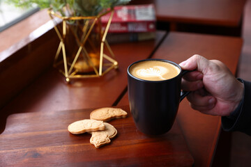 Hot Cappuccino coffee with black cup on old wooden table with isolate in black background