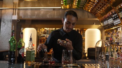 Portrait good looking Asian bartender using jigger measure liquor syrup into mixing glass preparation at luxurious beverage counter bar, neat professional barman costume at nightclub luxury. Vinosity.