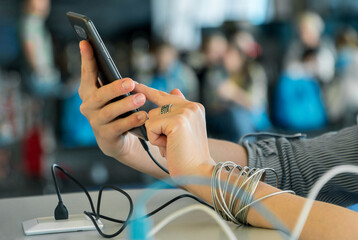 Close up of female hands charging smartphone using cord and usb plug in a public space while using...