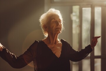 A senior woman stands in front of a window, hands extended to gaze outside