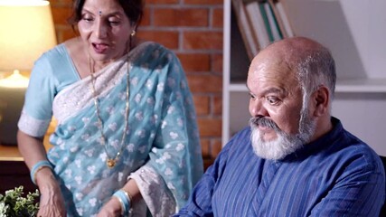 Happy Indian Asian senior couple celebrating  big rise in their investment while they joyfully look at a graph showing their stock market success, feeling proud and excited - Powered by Adobe