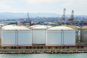 Many large round white reservoirs of chemical products in the port industrial terminal tank farm