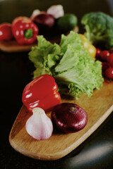 High angle shot of wooden plate with fresh bell pepper, lettuce and red onion