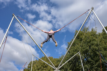 Young child from behind has fun jumping on a bungee trampoline high up to the sky, leisure outdoor activity on a festival, copy space